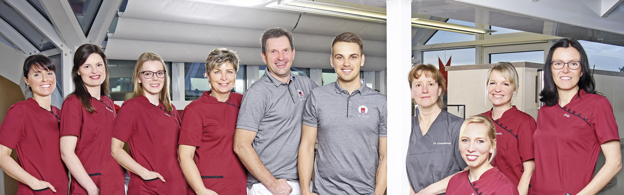 Gruppenbild: Das Team der Praxis für Implantologie und Oralchirurgie Dr. Jens Stoltz steht im Empfangsbereich der Praxis.